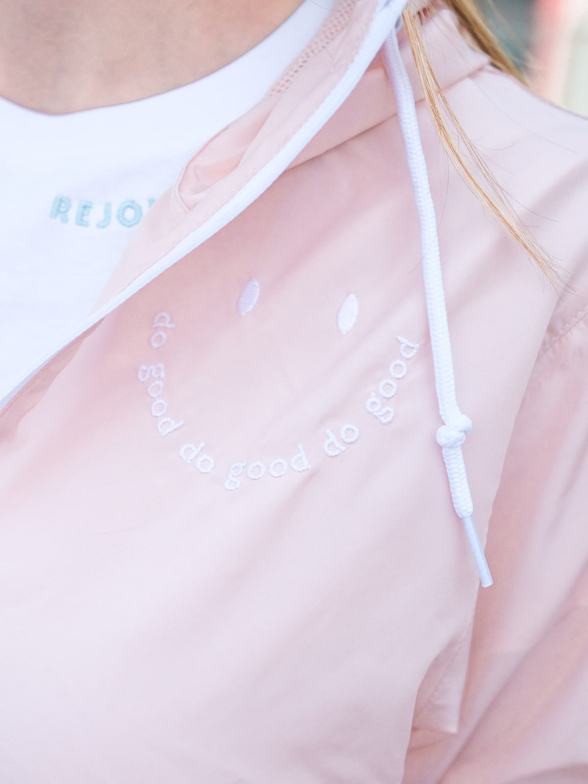 Blush Pink Windbreaker with a white zipper and a happy face embroidered on it. The happy face has the words "do good" written on it. This Christian women's jacket is based on Ecclesiastes 3:12 and our brand name Rejoice & Do Good
